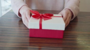 Genç ve çekici bir kadının elleri, güzel kırmızı ve beyaz bir kutuda partnerine yay ya da sevdiği birine hediye uzatır. Yıldönümü için romantik sürpriz konsepti, bir doğum günü