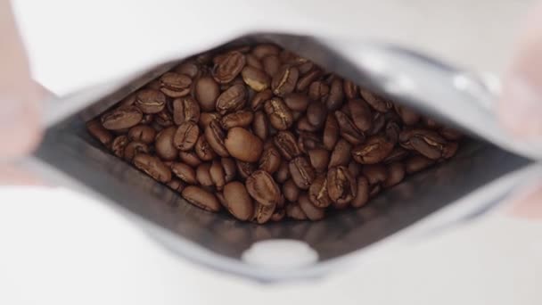 Mans händer öppnar ett paket nyrostat högkvalitativt kaffe, närbild av arabica kaffebönor. — Stockvideo