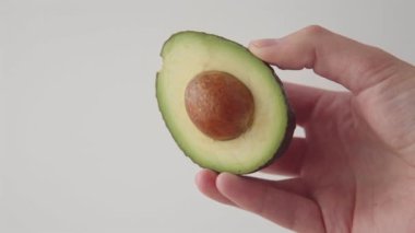 Beyaz arka planda kemik olan taze bir avokadonun yarısını dilimlenmiş bir elle tutuyorum. 4k görüntü.
