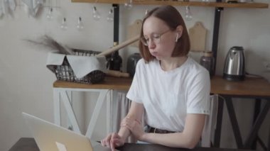 Kablosuz kulaklıklı modaya uyan iş kadını, videodaki konuşmacının sözlerine olumsuz tepki vererek, hayal kırıklığı içinde başını sallıyor, modern bir bilgisayarın önünde oturuyor.