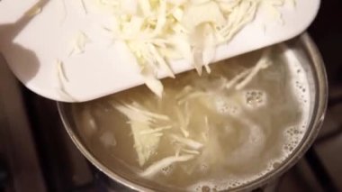 The process of cooking borscht - Ukrainian national dish. Shredded cabbage is poured into a pot of water.