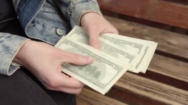 Kot ceketli bir adam para sayıyor. Yüzlerce dolarımız bir kızın elinde. Yakın çekim, 4K.