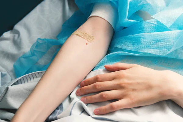 Close-up of a womans hand with a band-aid on her arm. Patient lying on a hospital bed after surgery. Intravenous injection, healthcare in a medical center.