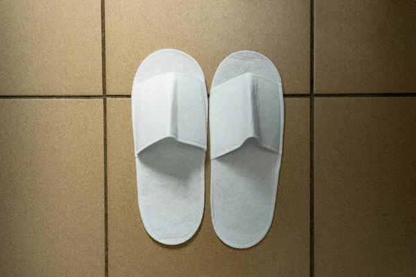 Disposable white slippers, guest shoes on the floor of the hotel or medical ward. Close-up shot.
