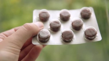 Gırtlak pastilleri siyah renkli, çikolata aromalı ve bulanık bir arka planda insan eli var..