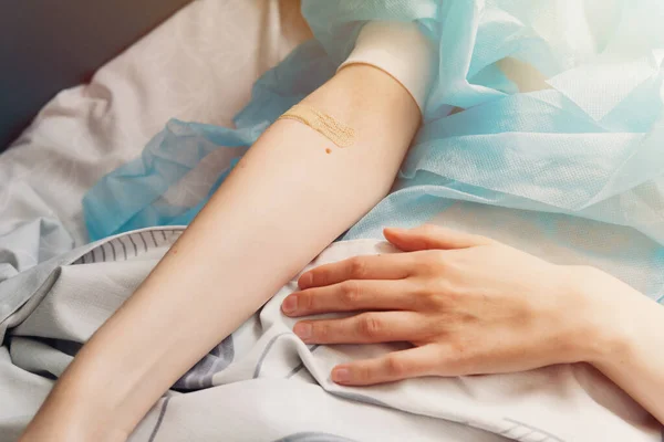 Close-up of female hand with a band-aid on her arm. Patient lying on a hospital bed after surgery. Intravenous injection, healthcare in a medical center.