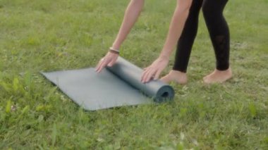 Close-up of of hands roll out yoga mat outdoors. A young woman, a strong successful sports coach, practices yoga and relaxes in the evening on the street.