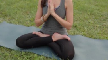 Relaxed female 20s 30s woman instructor meditating on yoga mat outside in city park with closed eyes in the evening.