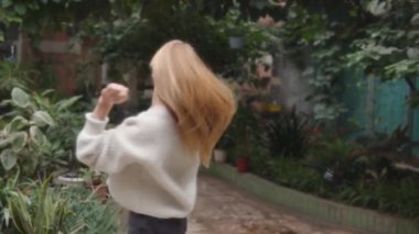 Genç sarışın bir kız beyaz yumuşak bir kazakla poz veriyor ve başarılı bir profesyonel fotoğrafçı bir serada çalışıyor. Yavaş çekim görüntüleri.