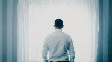 Pencerenin önünde duran depresif bir genç. Soğuk mavi tonlu çekim.