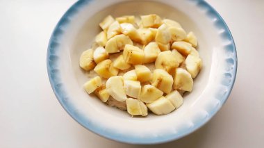 Dikey portre sağlıklı kahvaltı, yulaf lapası süt ve muz ile pan. Yulaf gevreği süt beyaz bir arka plan üzerinde bir çini tabak içinde dolu. Organik gıda kavramı güçlü kasları için.