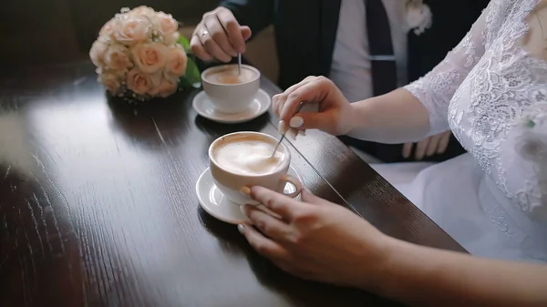 Young couple talking and drinking coffee during breakfast at cafe. They mixing sugar in cappuccino. Close up shot of hands.