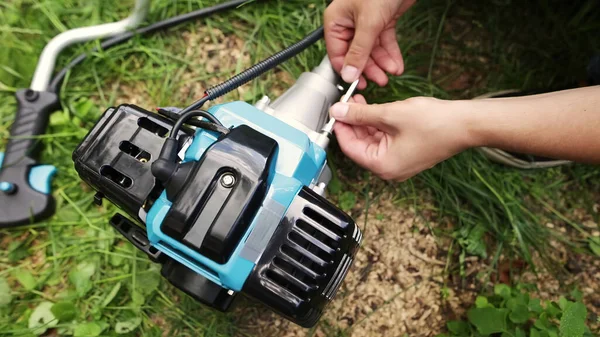 A man assembles parts of the brush cutter or string trimmer with a hex key on the grass, outdoors.