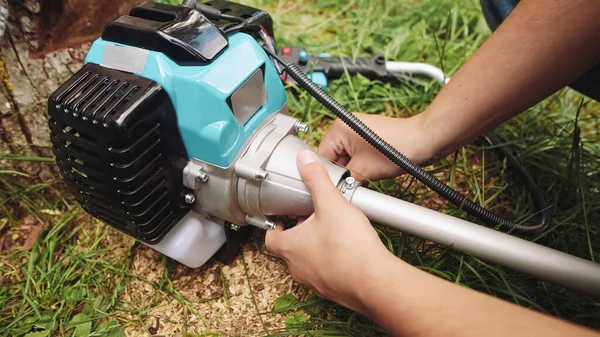 A man assembles brush cutter engine with a hex key on the grass, outdoors.