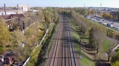 Güzel bir sonbahar şehrinin arka planında trensiz bir insansız hava aracı demiryolu üzerinde uçuyor. Havadan görünüşlü. Demiryolunda bir sürü vagon var. Tren istasyonunda. Ticari malların nakliyesi