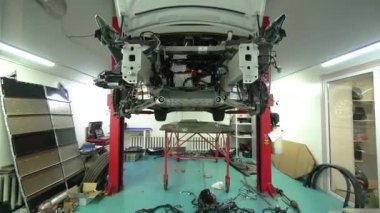 Parçalanmış elektrikli araba, motoru olmayan bir asansörde duruyor. Profesyonel otomotiv tamircisi, garajda sökülmüş aletleri kullanarak arabaları kontrol edip tamir ediyor. Araba servisi, bakım konsepti