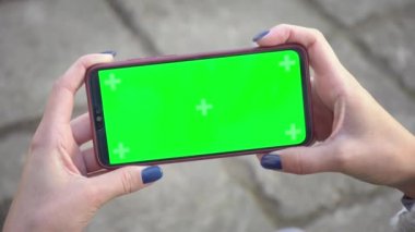 Kadın cep telefonunu tutuyor ve ekranda tıkırdıyor kaldırım taşlarının arka planında fotoğraflar ya da fotoğraflar çekiyor. Chroma tuşu elinde akıllı telefondan model alınıyor. Kopyalama alanı için yeşil ekran kullan 4k
