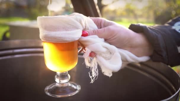 El jugo de manzana recién exprimido se vierte en un vaso que es sostenido por una niña con gotitas en el vaso al atardecer. Preparación de zumo de manzana fresco con una prensa de fruta vieja. Concepto de comida saludable — Vídeos de Stock