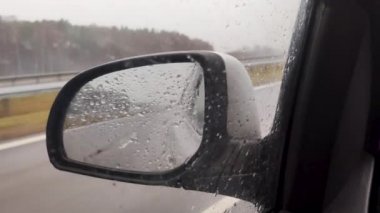 View car side mirror at rain. Raindrops on car side. Traveling in bad wet weather.