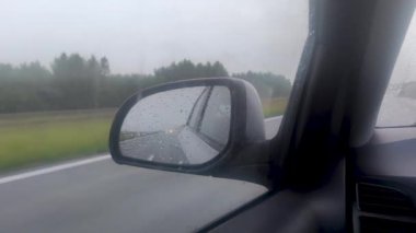 Car wing mirror view during a heavy rainy drive.