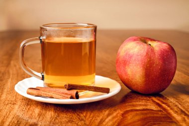 Cam bardakta çay poşeti, tarçın çubuğu ve kırmızı elma.