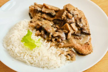 Lezzetli mantar soslu domuz eti ve beyaz tabakta pilav.