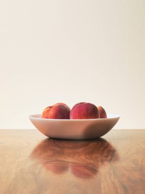 Still life with peach fruit and white bowl on wooden table