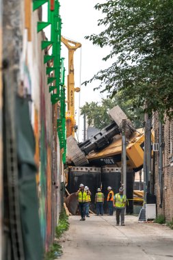 Chicago, IL - 6 Ekim 2021: İnşaat işçileri, Bryn Mawr CTA tren istasyonu yakınlarında çalışırken bir inşaat yığını sondaj kulesi devrildikten sonra ara sokakta toplandılar.