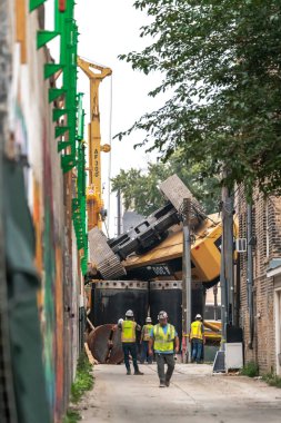 Chicago, IL - 6 Ekim 2021: İnşaat işçileri, Bryn Mawr CTA tren istasyonu yakınlarında çalışırken bir inşaat yığını sondaj kulesi devrildikten sonra ara sokakta toplandılar.