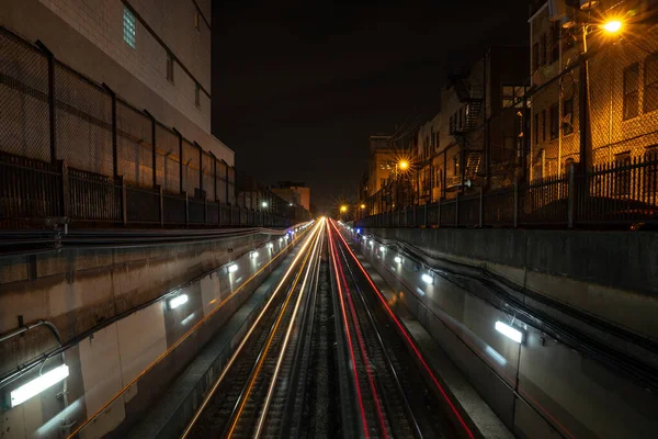 線路の両側に路地の照明や住宅のある夜に地下トンネルから出発し 来るCta列車からの長い露出白と赤の光の道 — ストック写真