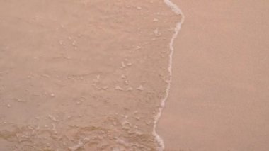 Yavaş çekim aşağı doğru süzülüyor dalgalar bir göldeki kumsala vuruyor kabarcıklar yaratıyor ve kıyıya vuruyor..