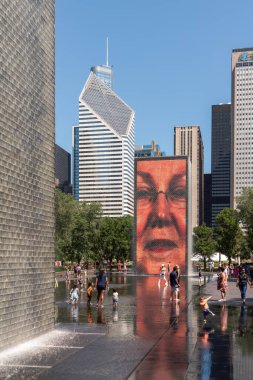Chicago, IL - 12 Temmuz 2022: Çocuklar sıcak bir yaz gününde şehir merkezindeki bir halk parkında çeşmeye su sıçratır ve havuzu yansıtırlar..