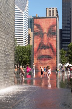 Chicago, IL - July 12th, 2022: Children play and splash around in the water fountain and reflecting pool in a public park downtown on a hot summer day.