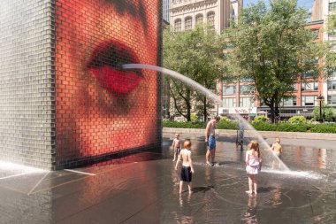 Chicago, IL - July 12th, 2022: Children play and splash in the water fountain and reflecting pool in a public park downtown as water shoots out of the towers on a hot summer day.