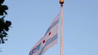 Chicago bayrağını yakından çekerken mavi beyaz çizgili ve kırmızı yıldızlı uzun bir bayrak direğinde sallanırken altın saat günbatımında şehir merkezindeki bir müze binasında..