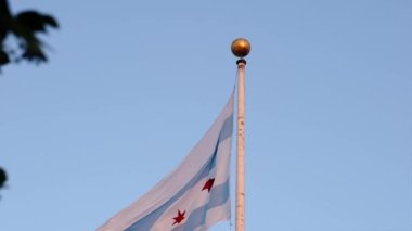 Chicago bayrağını yakından çekerken mavi beyaz çizgili ve kırmızı yıldızlı uzun bir bayrak direğinde sallanırken altın saat günbatımında şehir merkezindeki bir müze binasında..