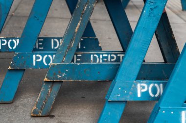 Close up view of several stacked weathered and worn blue wooden road barricade A-frame legs with Police Department written on them as they sit on a concrete sidewalk in New York City.