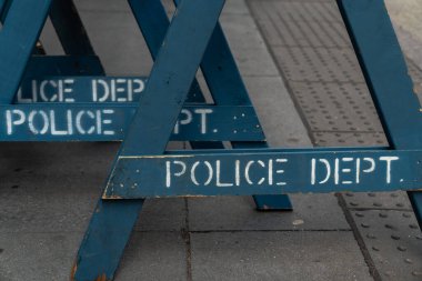 Close up view of several stacked weathered and worn blue wooden road barricade A-frame legs with Police Department written on them as they sit on a concrete sidewalk in New York City.