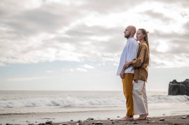 Genç ve sevgi dolu bir çift sahilde ayakta durup sarılıyor. Görüntü, çift ilişkisinin samimiyetini gösteriyor. Görünüşe göre o çift öpüşmek üzere. Yüksek kalite fotoğraf. Bulutlu hava.