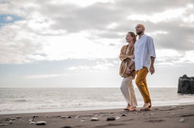 Genç ve sevgi dolu bir çift sahilde ayakta durup sarılıyor. Görüntü, çift ilişkisinin samimiyetini gösteriyor. Görünüşe göre o çift öpüşmek üzere. Yüksek kalite fotoğraf. Bulutlu hava.