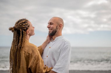 Genç ve sevgi dolu bir çift sahilde ayakta durup sarılıyor. Görüntü, çift ilişkisinin samimiyetini gösteriyor. Görünüşe göre o çift öpüşmek üzere. Yüksek kalite fotoğraf. Bulutlu hava.