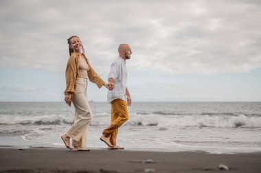 Genç ve sevgi dolu bir çift sahilde ayakta durup sarılıyor. Görüntü, çift ilişkisinin samimiyetini gösteriyor. Görünüşe göre o çift öpüşmek üzere. Yüksek kalite fotoğraf. Bulutlu hava.