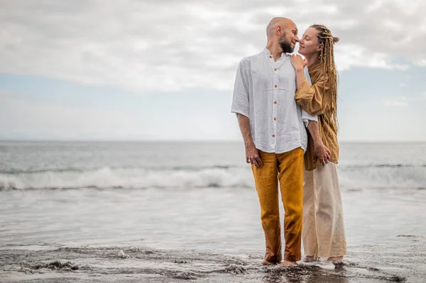 Genç ve sevgi dolu bir çift sahilde ayakta durup sarılıyor. Görüntü, çift ilişkisinin samimiyetini gösteriyor. Görünüşe göre o çift öpüşmek üzere. Yüksek kalite fotoğraf. Bulutlu hava.
