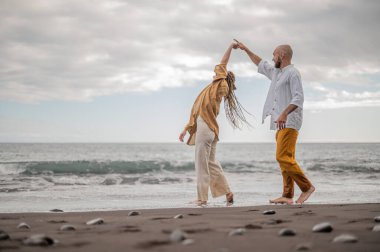 Kumsalda el ele tutuşan, kumsalda yürüyen genç bir çift. Yüksek kalite fotoğraf. Bulutlu hava.