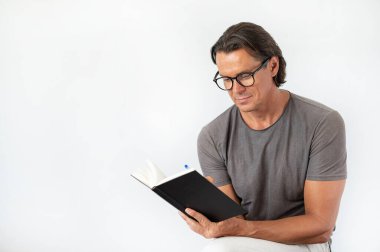 Olgun, başarılı ve eğitimli gözlüklü bir adam ve beyaz bir kitap okuyor.