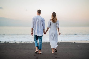 Genç bir çift gün batımında sahilde yürüyor ve el ele tutuşuyorlar, arkadan görüyorlar, beyazlar içinde, tarih ya da yıldönümü