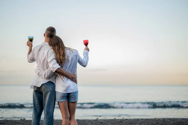 Pareja Joven Abrazándose Una Playa Atardecer Mirando Mar Sosteniendo Una — Foto de Stock