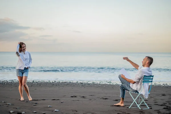 Pareja Joven Una Playa Atardecer Ella Posa Dibuja Foto Alta — Foto de Stock