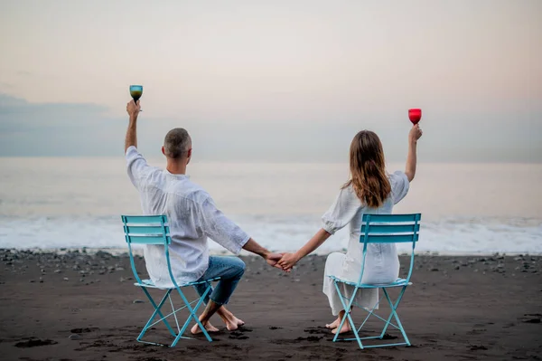 Young Couple Holding Hands Sitting Beach Sunset Looking Sea Holding — Stock Photo, Image