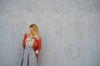  Gri bir duvara karşı parlak gömlekli ve etekli genç bir kız.